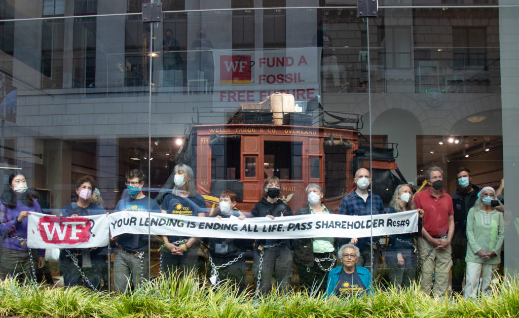 A photo of the protesters in chains, holding a banner that says "WF your lending is ending all life. Pass shareholder res #9"